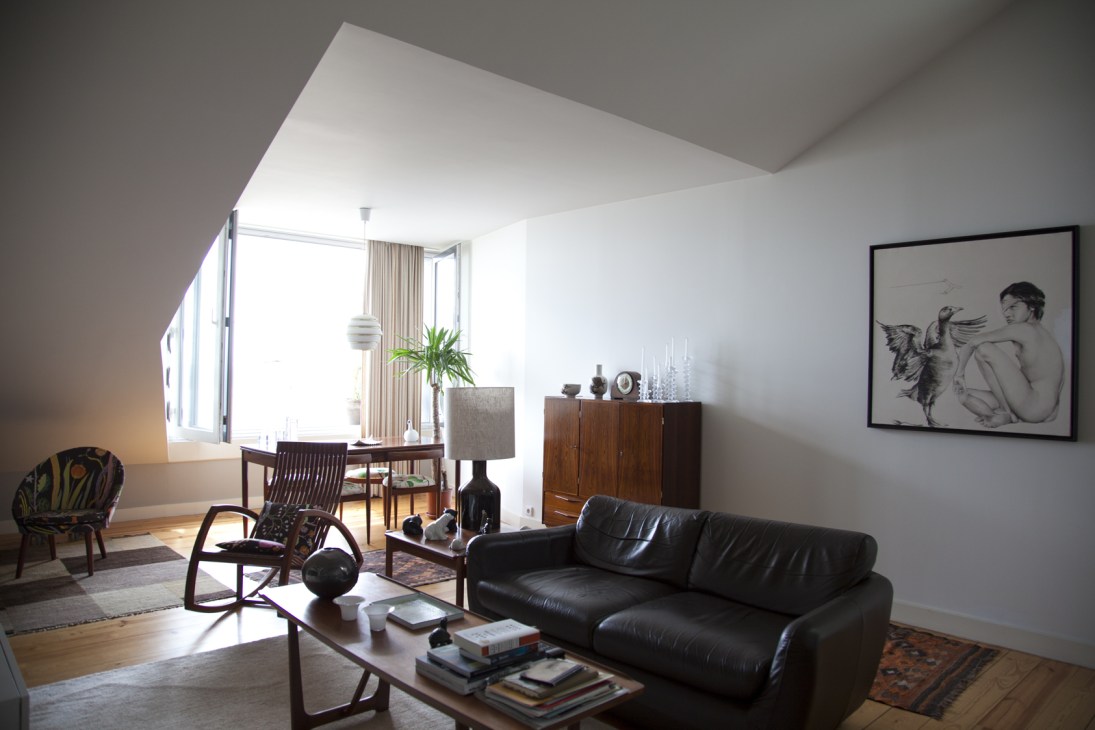 Contemporary living room with black leather sofa, mid-century furniture, and framed artwork on white walls.