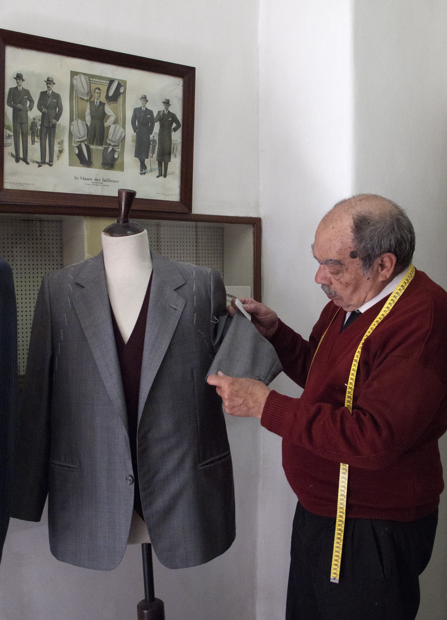 Tailor Júlio Lafuente adjusting a grey suit on a dress form in his shop.