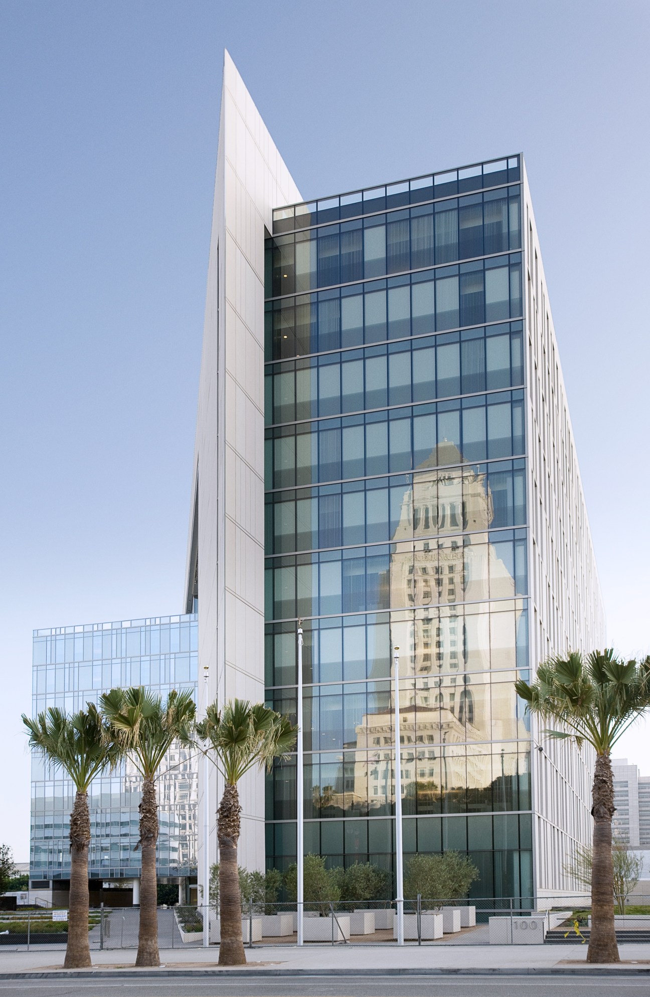 Modern glass and white facade of LAPD Police Administration Building in downtown Los Angeles with palm trees.