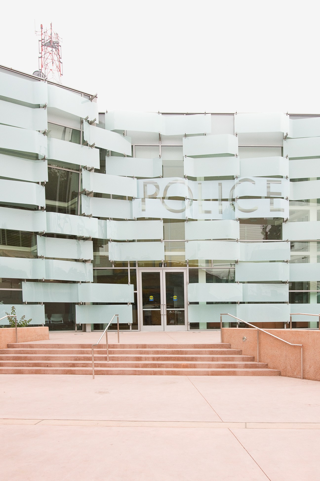 Modern LAPD Hollenbeck Police Station with glass and white panel facade and pink plaza entrance.
