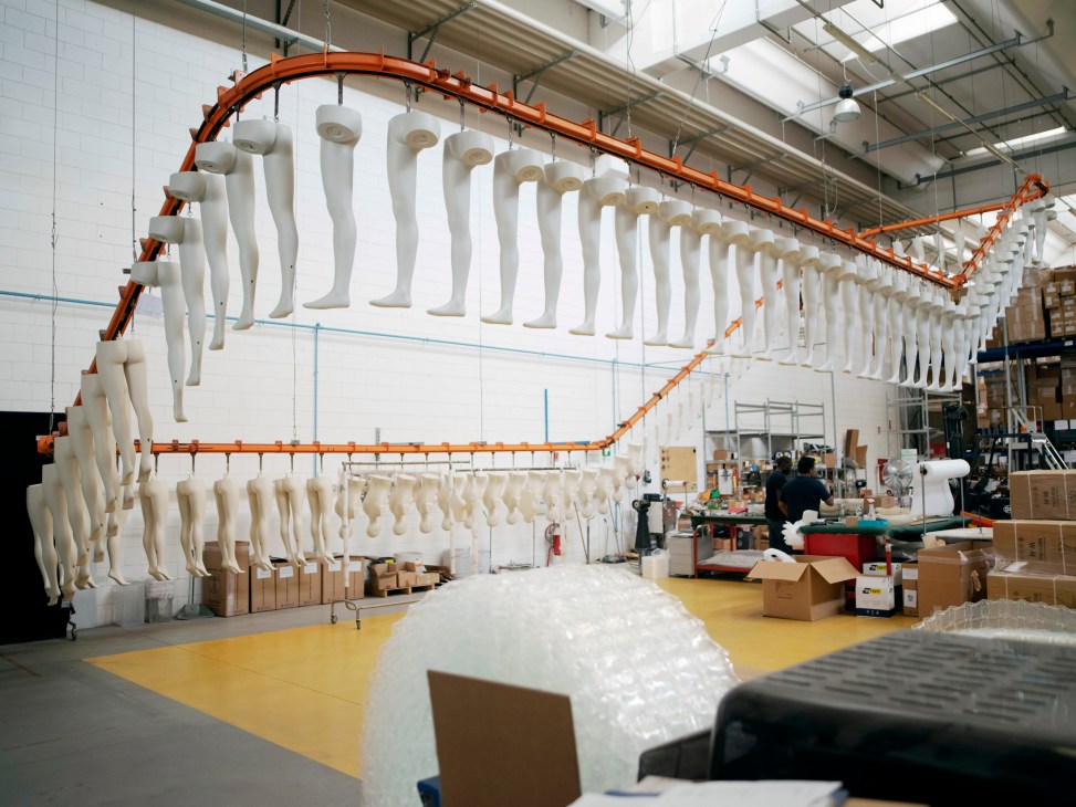Mannequin legs and torsos hanging on an orange conveyor system in La Rosa's production facility for drying.