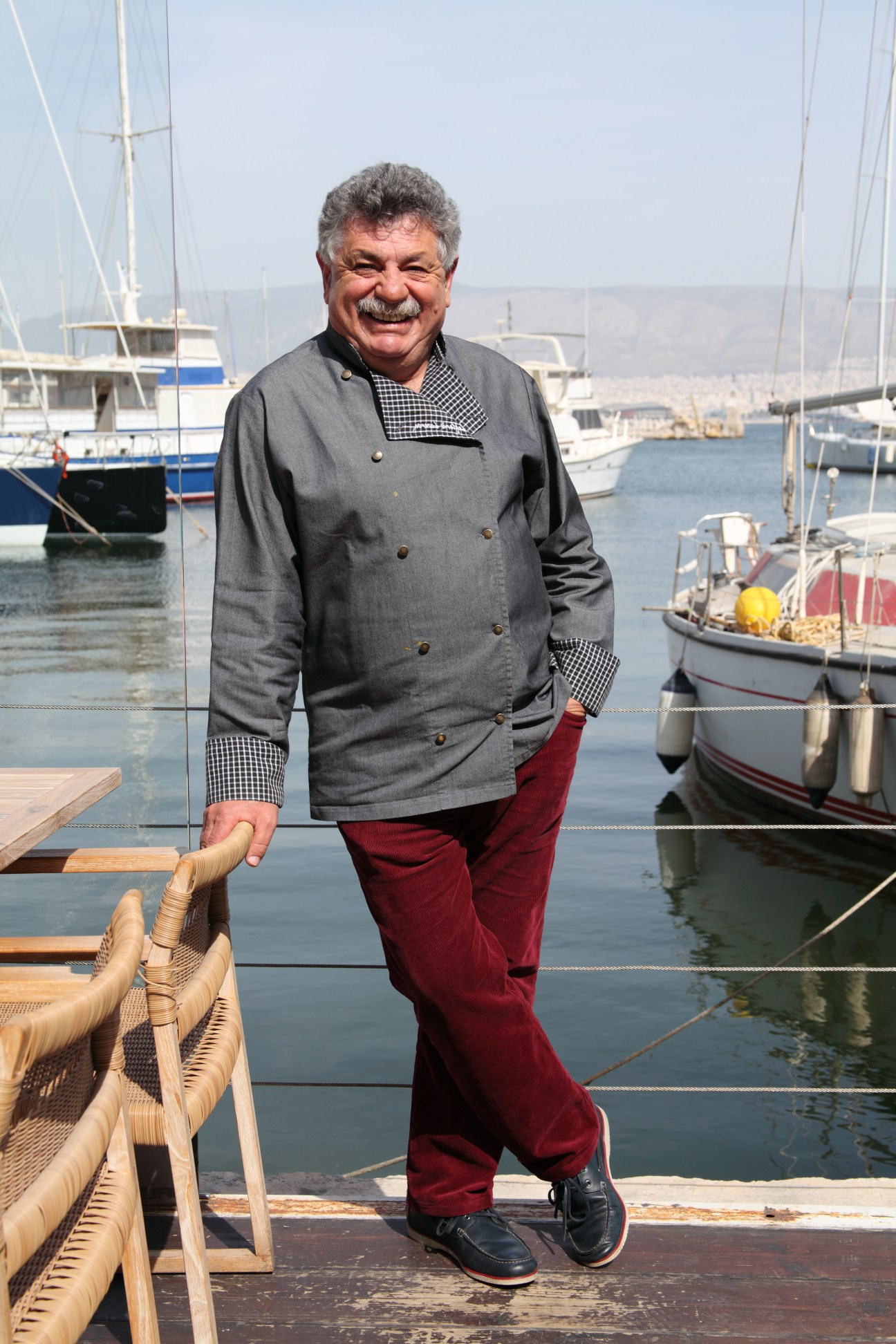 Chef Lefteris Lazarou standing on a dock with sailboats and harbor in the background.