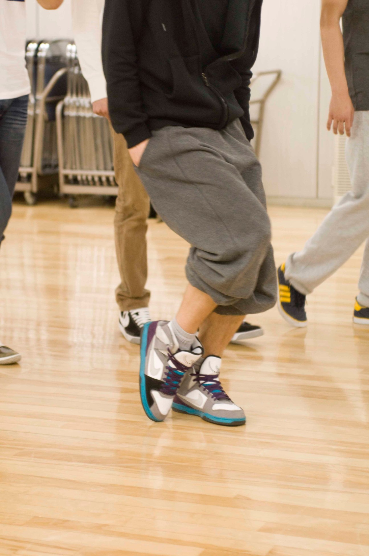 A dancer demonstrates choreography moves in a studio wearing colorful sneakers on a wooden floor.
