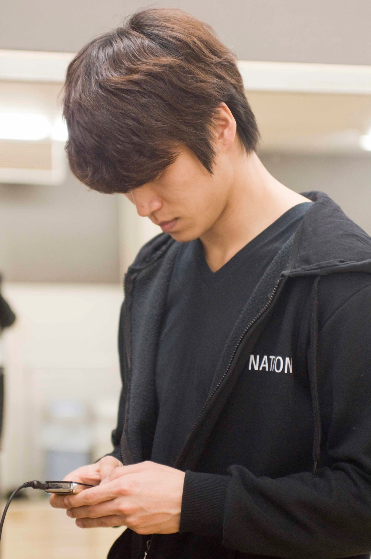 Man in black jacket looking at mobile phone in studio setting.