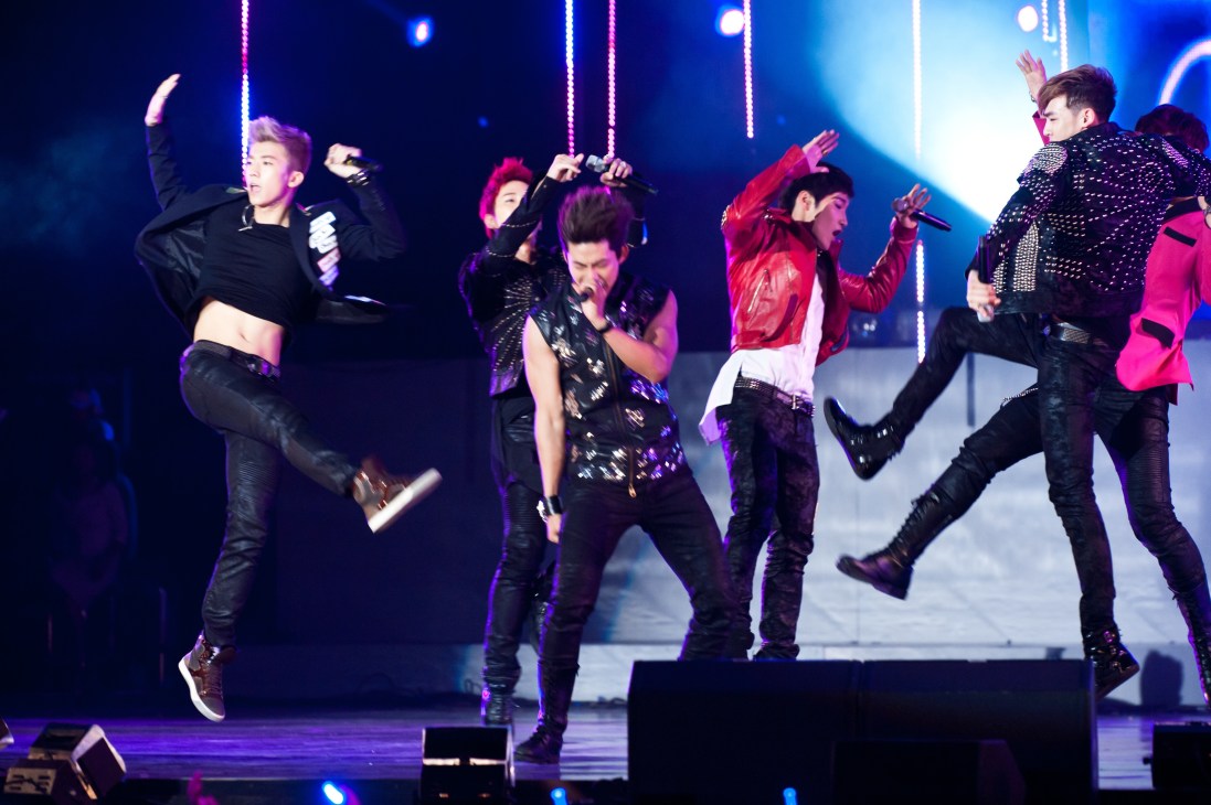 K-pop band 2PM performing on stage with dynamic choreography and colorful stage lighting.