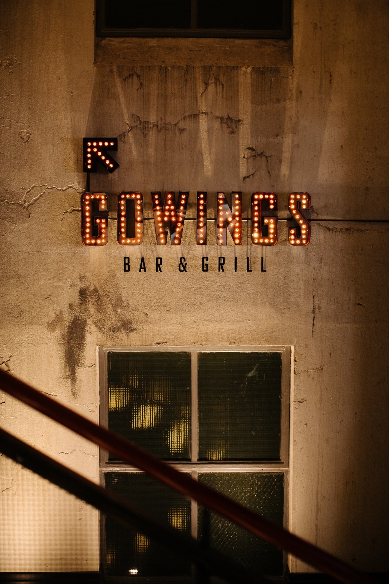 Illuminated neon sign reading 'Gowings Bar & Grill' on a weathered concrete wall at night.
