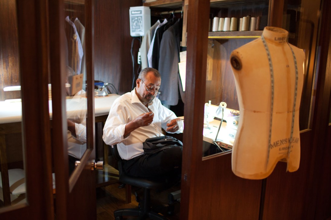 Tailor working at a fitting station with dress forms and fabric samples at Noir, Le Lis menswear store.