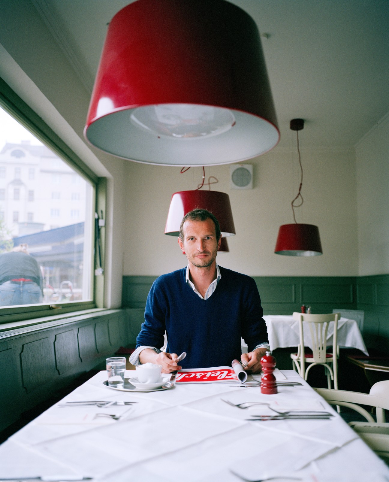 Markus Huber, editor of Fleisch magazine, sits at a table in a bright café with red pendant lamps.