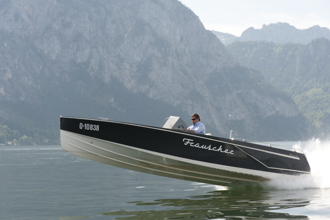 Black and white Frauscher motor boat with man at helm on Alpine lake with mountains.