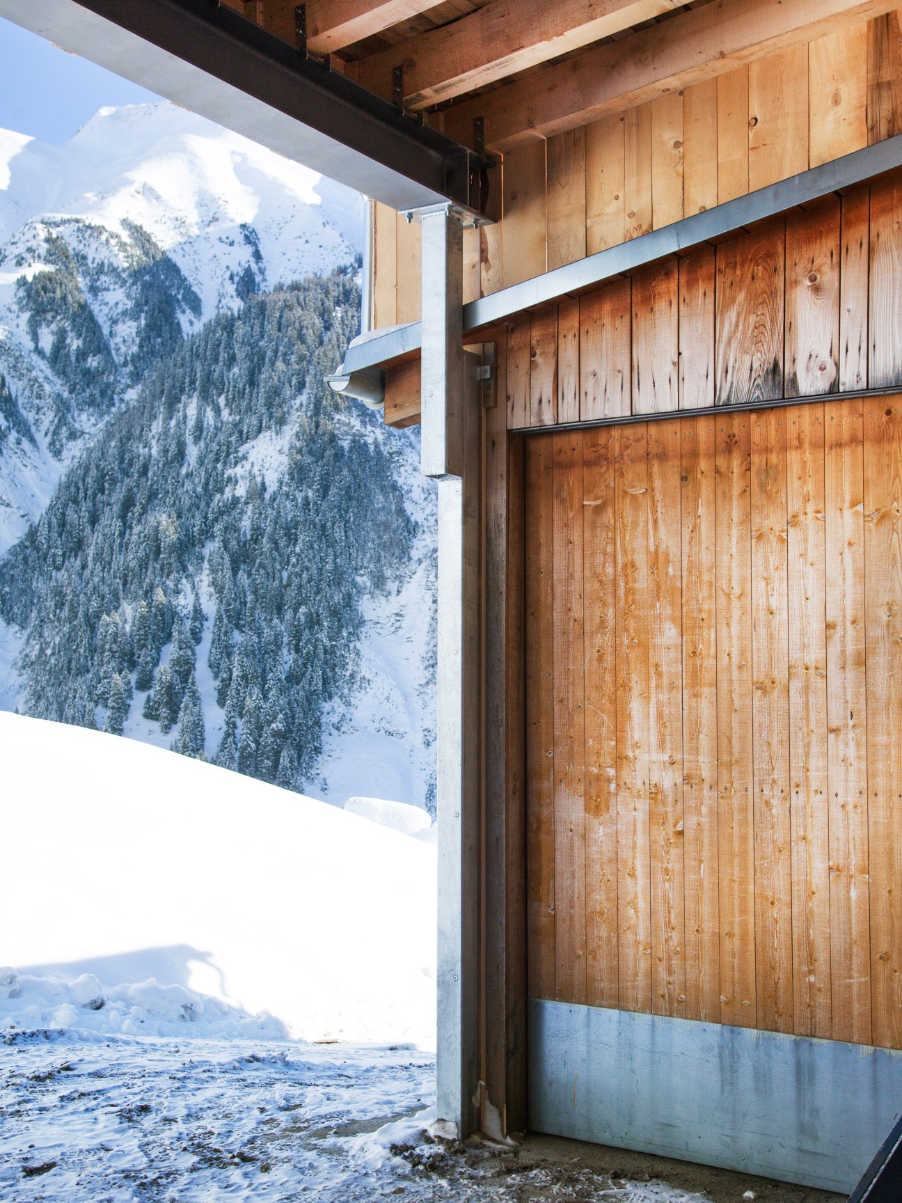 Wooden barn interior with snowy Alpine mountain vista visible through open doorway.