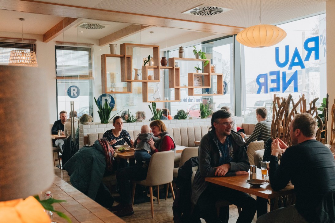 Diners enjoy meals at modern restaurant Rauner in Linz with contemporary wooden shelving and large windows