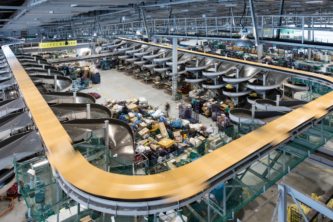 Overhead view of Hong Kong International Airport's Air Mail Centre showing automated sorting systems and stacked cargo parcels.