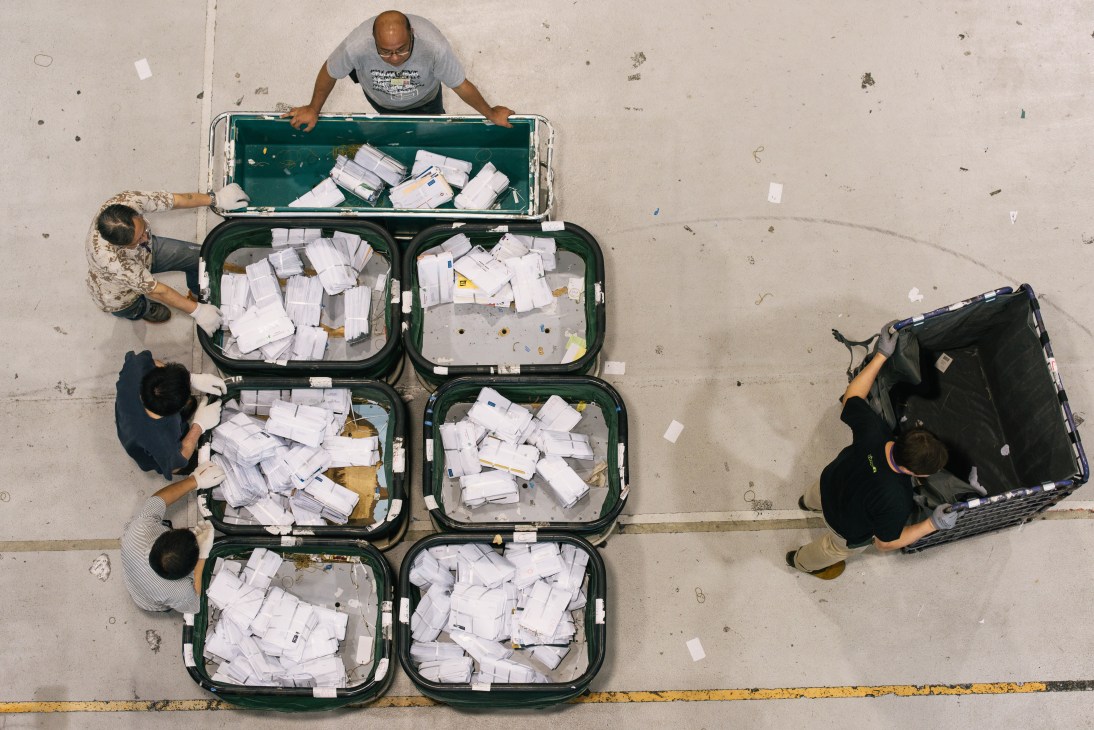 Workers sort white mail packages into green containers at Hong Kong International Airport's Air Mail Centre.