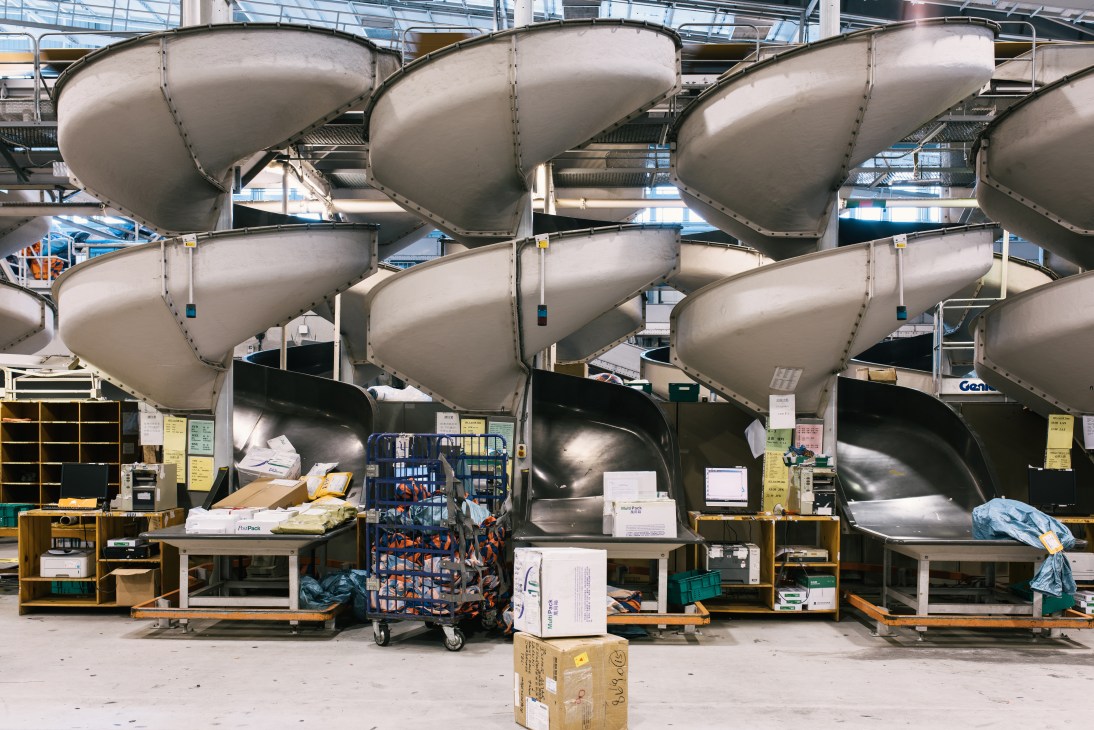 Large silver air cargo containers stacked in rows at an airport terminal with work stations and equipment below.
