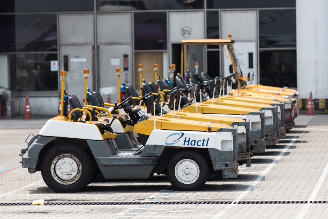 Row of yellow and grey Hactl tow tractors parked at Hong Kong International Airport apron.
