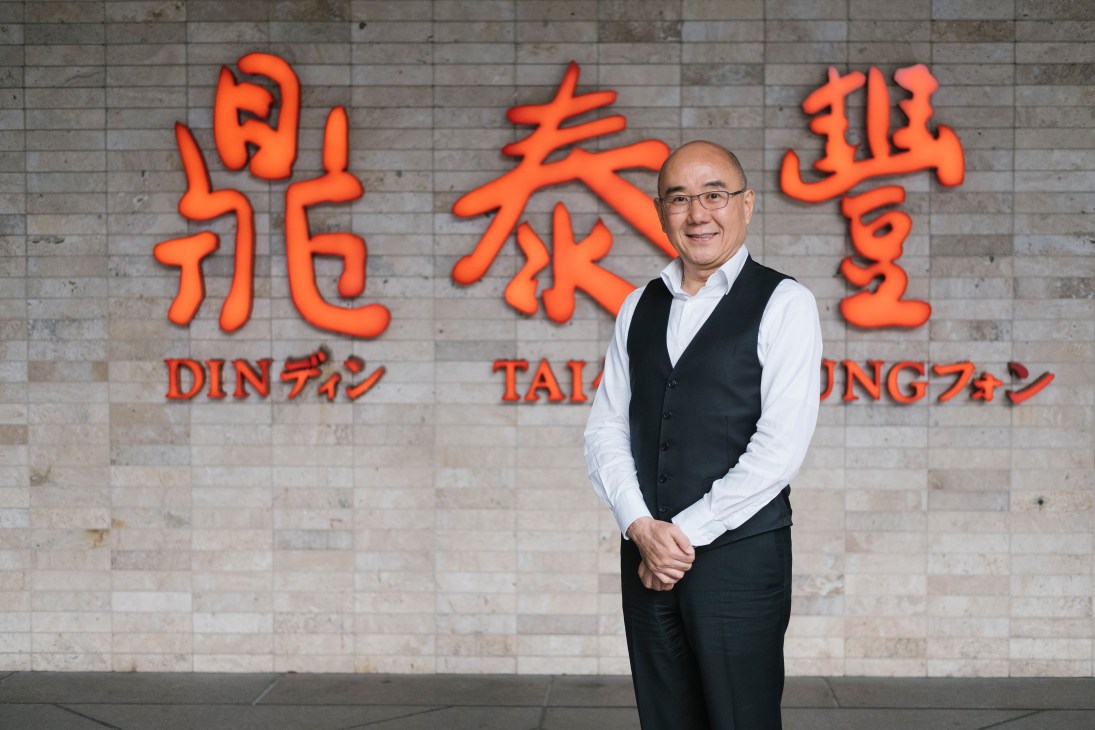 Warren Yang, CEO of Din Tai Fung, stands in front of the restaurant's illuminated orange signage.
