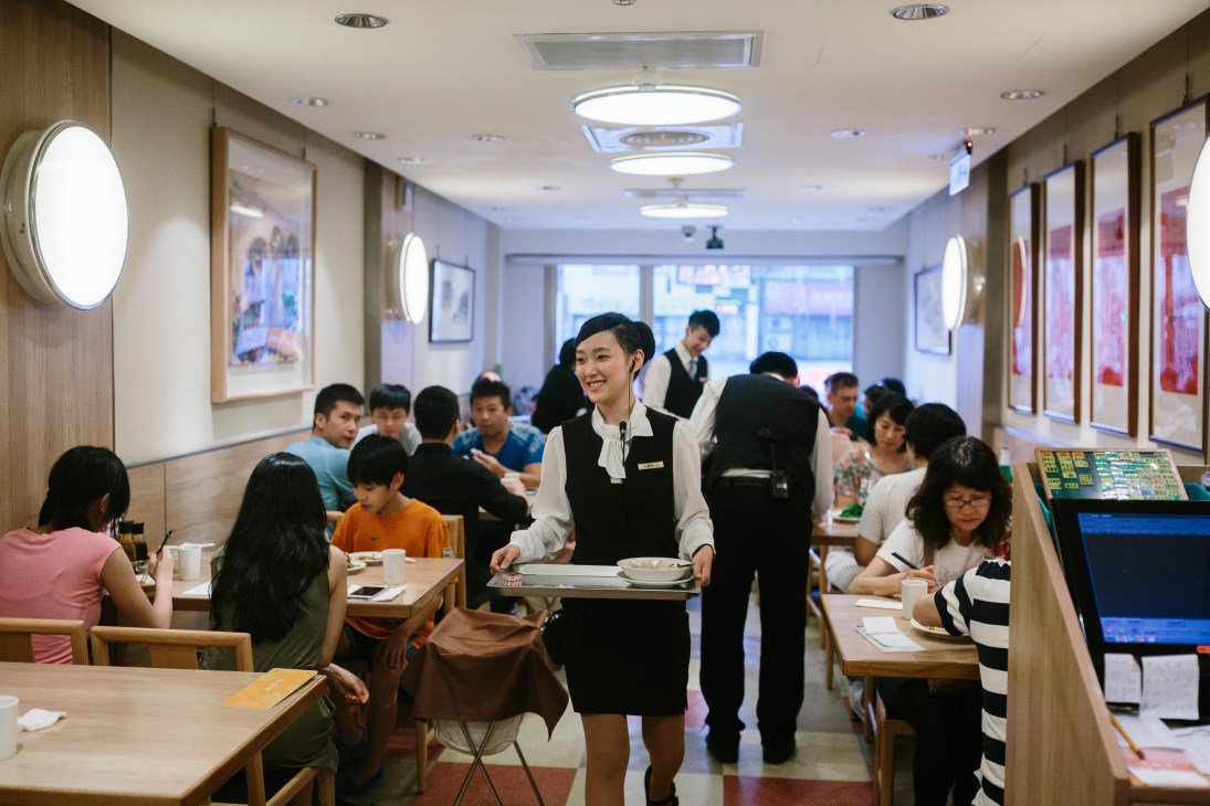 Din Tai Fung waitstaff serve customers in a modern dining room with warm lighting.