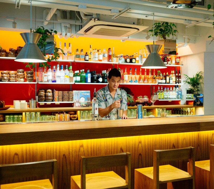 Bartender preparing a drink at Potato Head's bar in Hong Kong with colorful shelving behind.