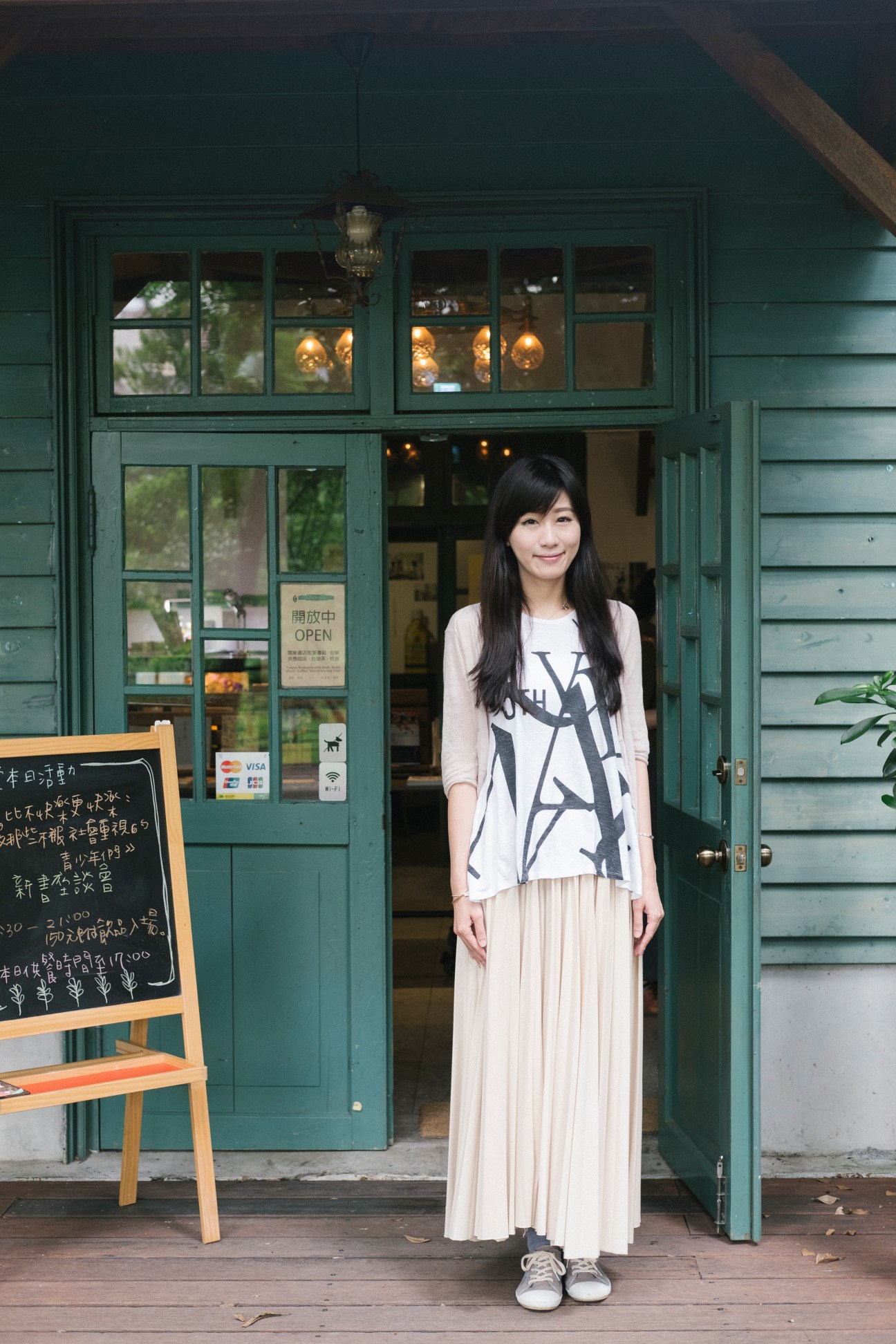 Woman standing in front of Yue Yue & Co bookshop with green wooden doors