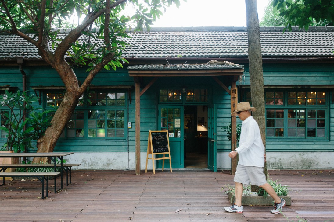 Man in white shirt and hat jogging past Yue Yue & Co bookshop with turquoise exterior and traditional tile roof.
