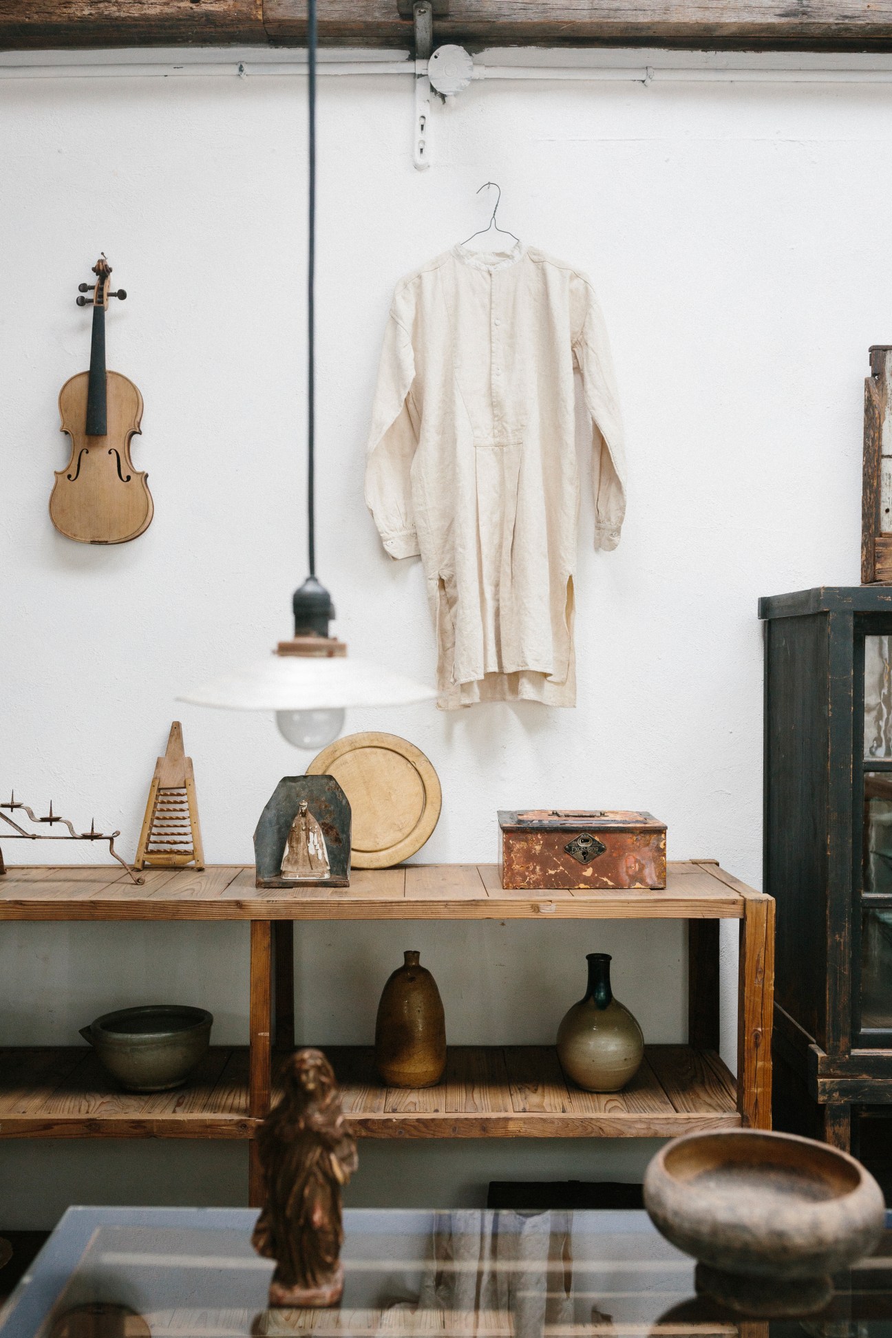 Interior of Antique Delicate design shop displaying vintage items including a violin, cream linen garment, wooden bowls, and metalware on shelves.