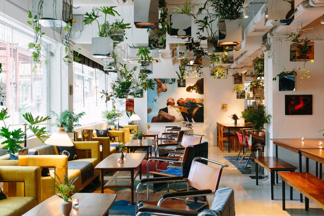 Interior of Potato Head restaurant in Hong Kong with hanging plants, yellow seating, and artwork on walls.