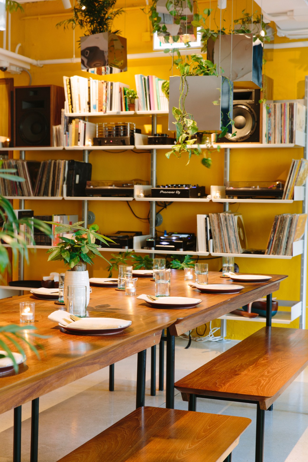 Interior of Potato Head restaurant in Hong Kong with bright yellow walls, wooden dining table, shelving with books and plants.