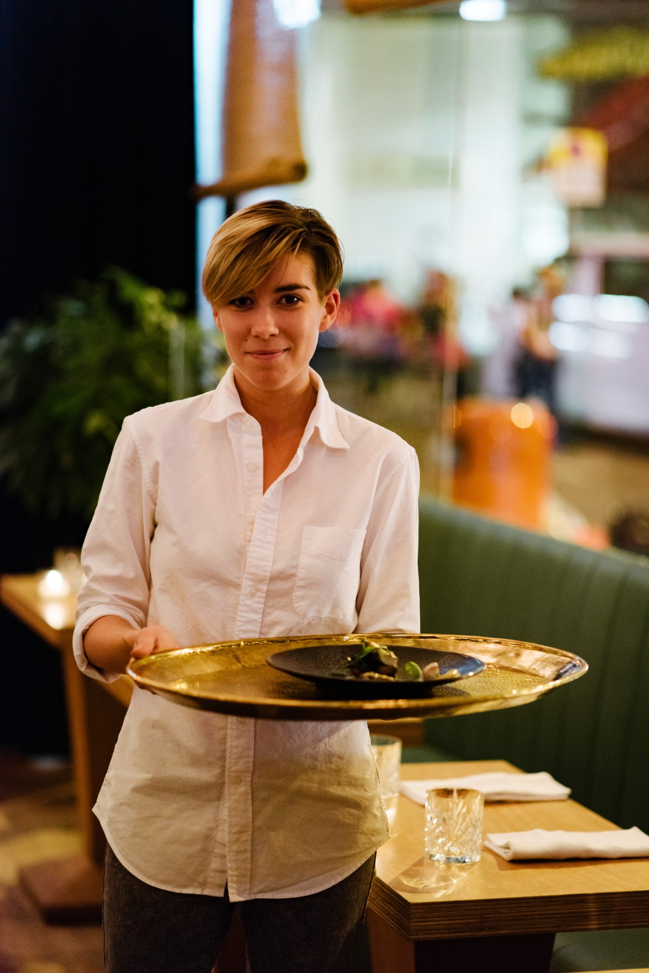 Server in white shirt holding a gold plate with food at Serge et Le Phoque restaurant.