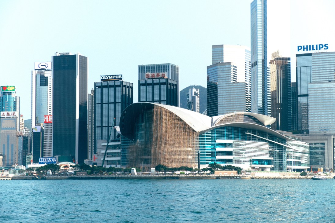 Hong Kong Convention and Exhibition Centre with partial bamboo scaffolding covering its distinctive curved architecture, waterfront skyline in background.