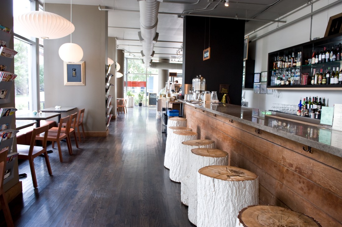 Interior of Little Branch Cafe showing wooden bar with stools, pendant lights, and shelved beverages.