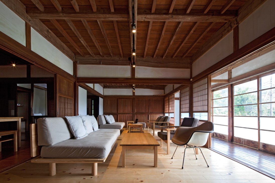 Modern Japanese living room with wooden beams, hinoki cypress flooring, Muji furniture, and sliding glass doors overlooking a lake.
