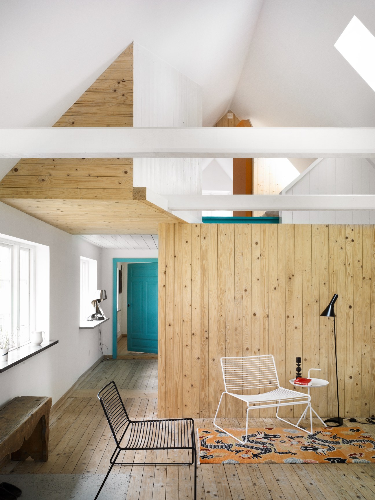 Interior of a holiday home with wooden ceiling beams, white walls, and a wooden partition wall with a turquoise door.