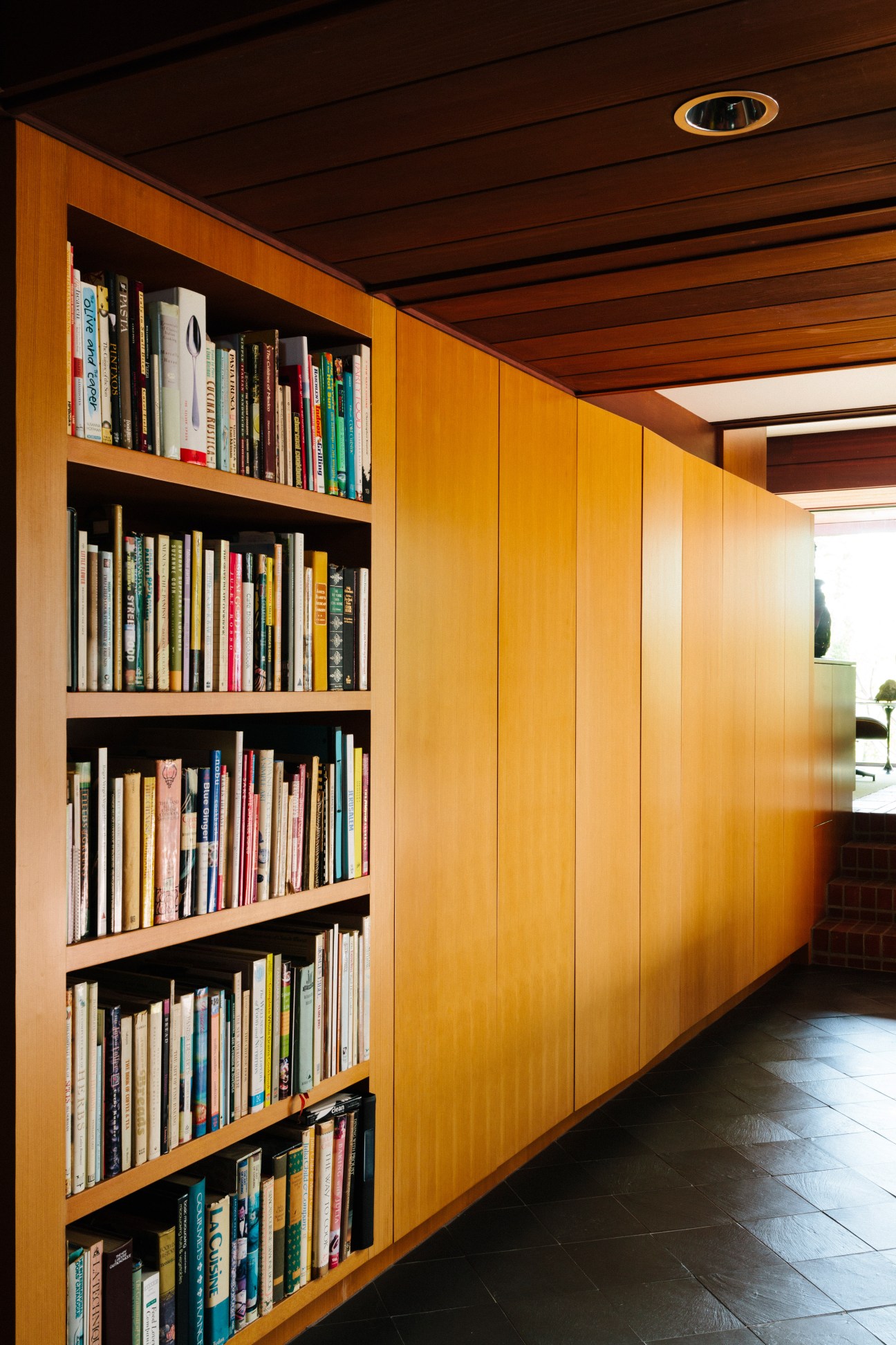 Douglas fir cabinets lining a passage with black shelving against warm wood paneling and French doors.