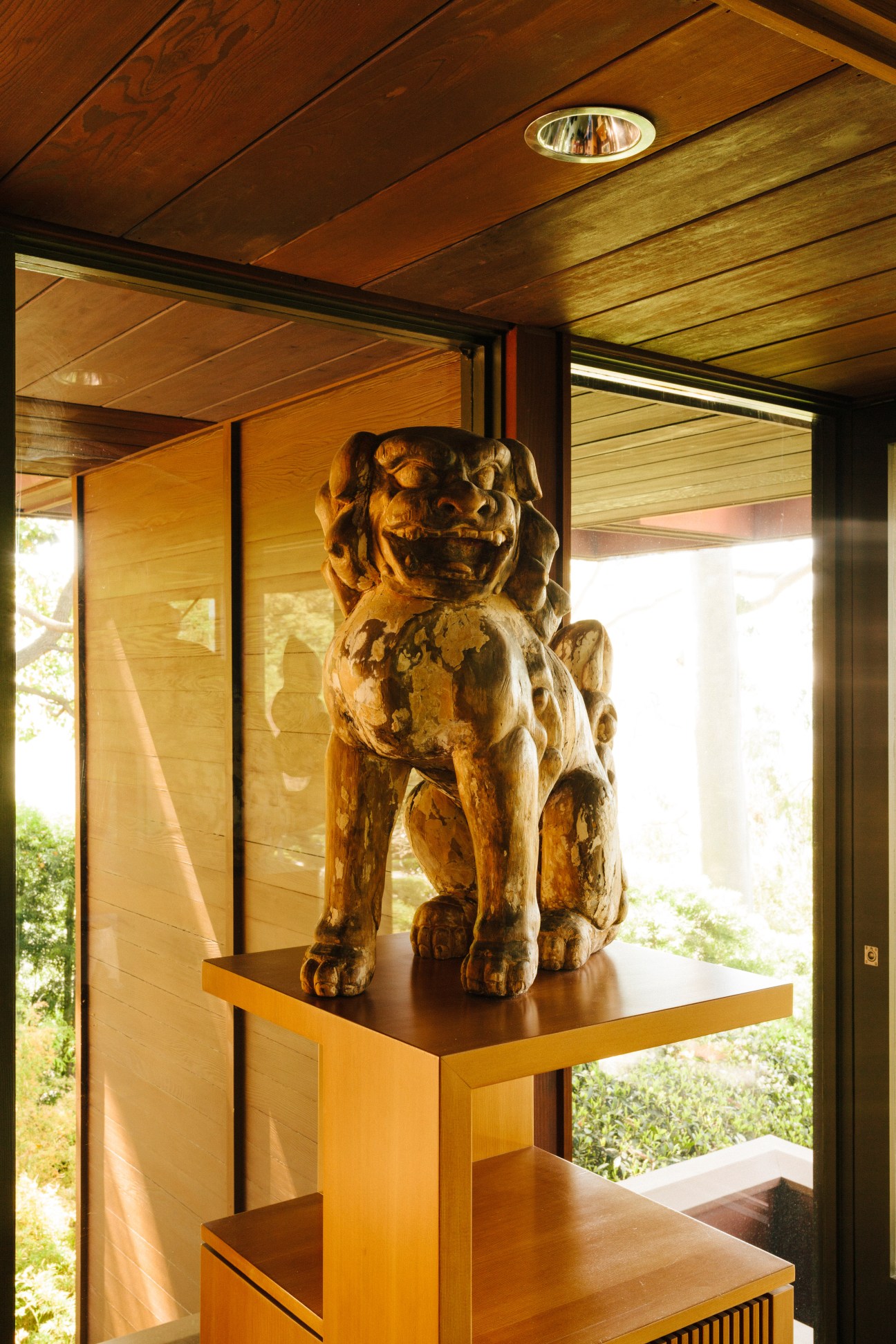 Wooden carved Chinese guardian lion statue on wooden pedestal in modernist home interior.