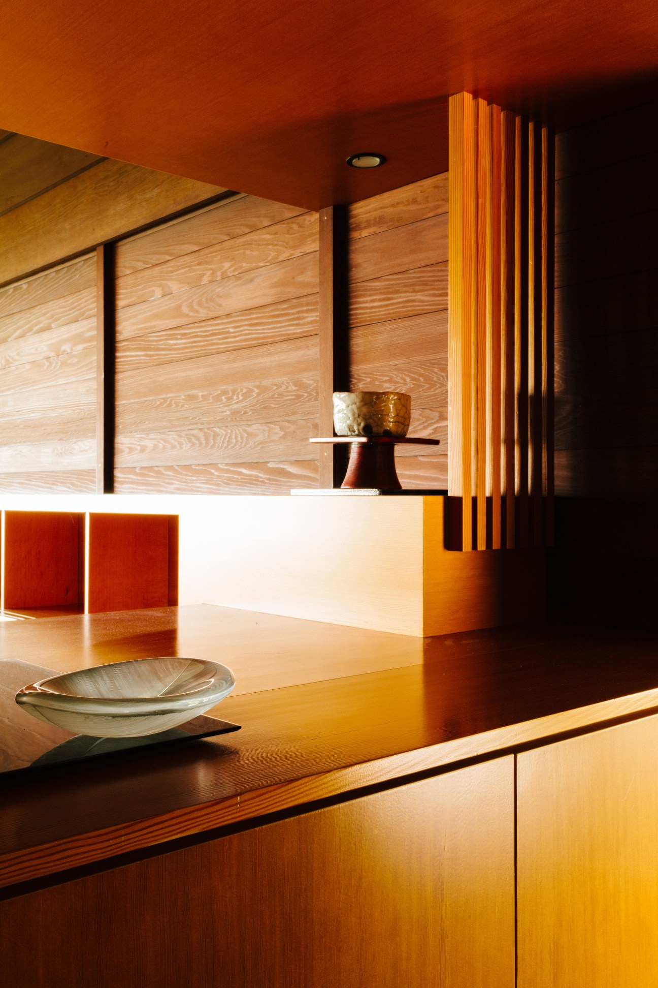 Modernist interior with warm wood tones, orange ceiling, white counter, and decorative bowl under natural light.
