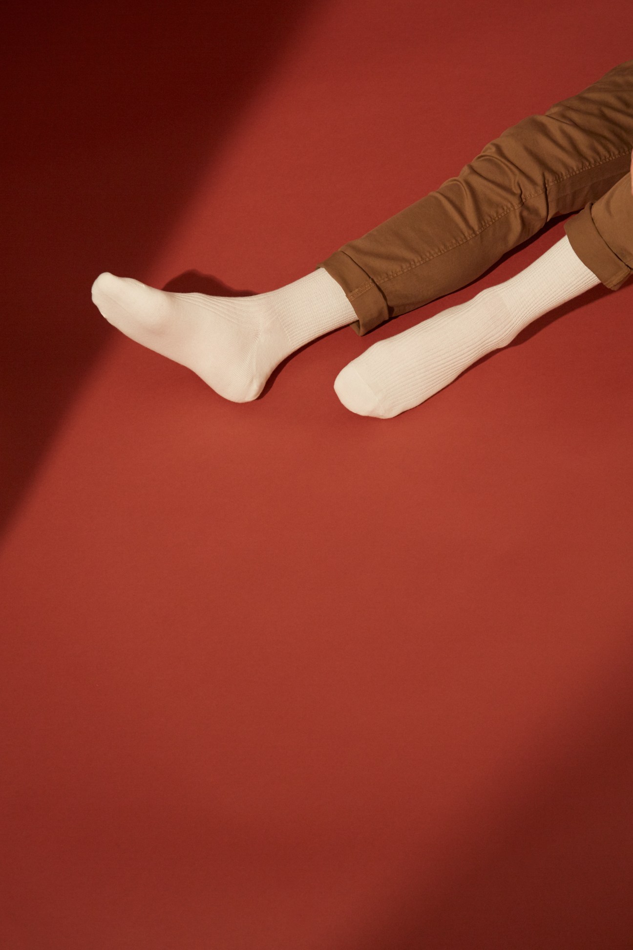 Person wearing white ribbed socks and brown trousers against a red background.