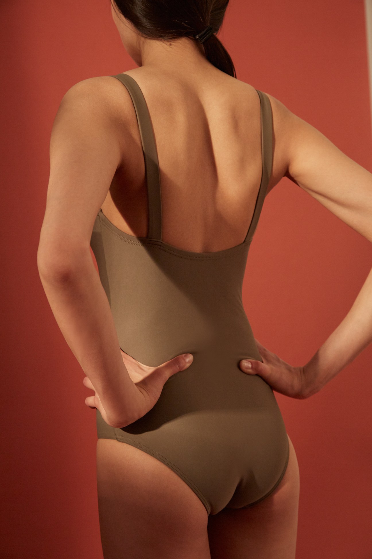 Woman wearing a beige Matteau swimsuit against a coral background.
