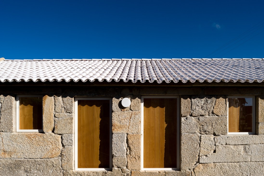 Modern mountain residence with white ceramic tile roof and granite stone walls featuring golden-yellow wooden doors.
