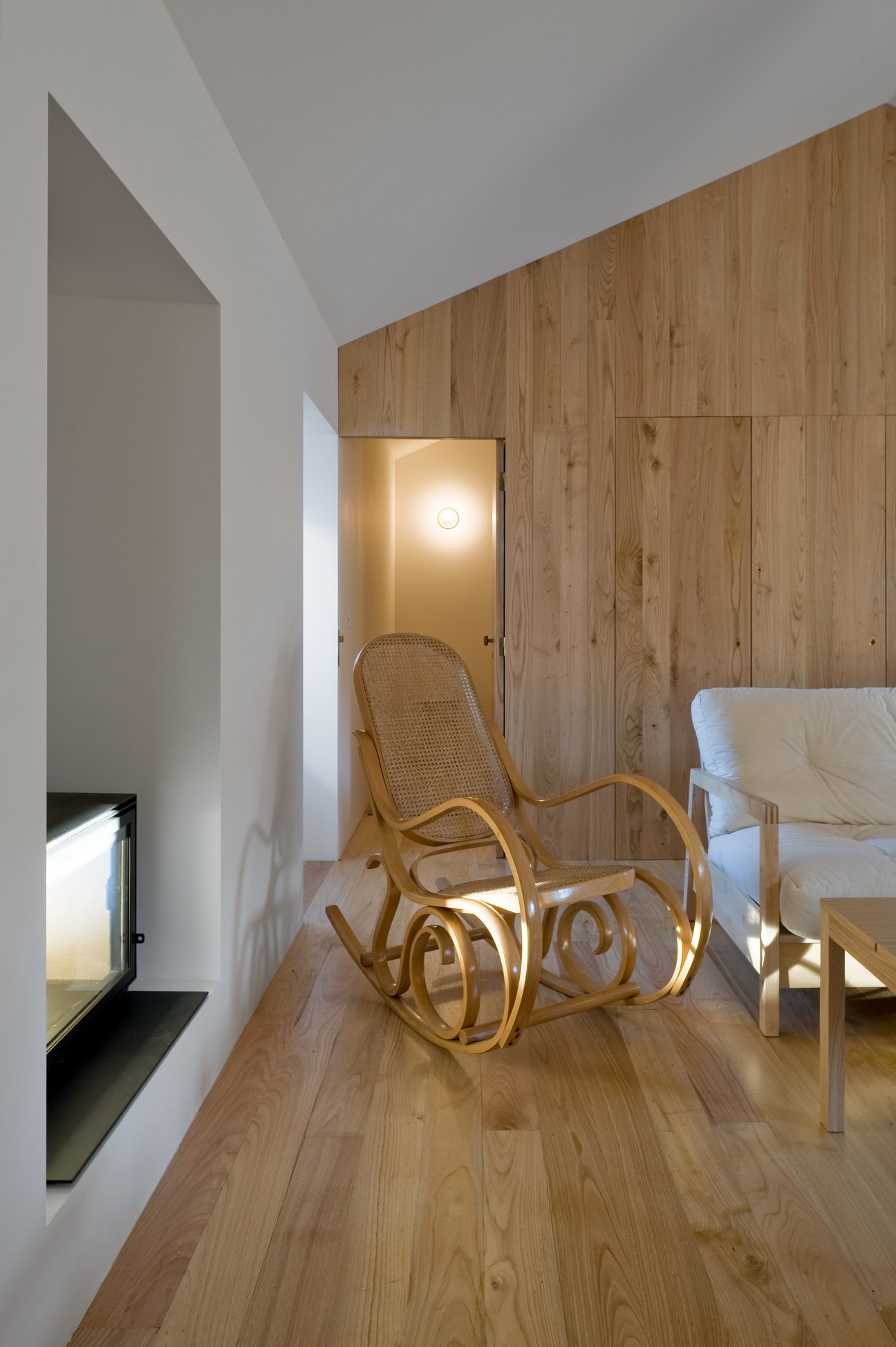 Modern minimalist interior with wooden walls, rocking chair, and built-in fireplace nook.