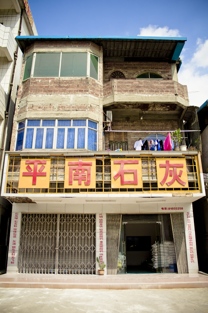 A weathered residential building in Chashan factory town with blue-roofed upper levels and Chinese signage on yellow storefront below.