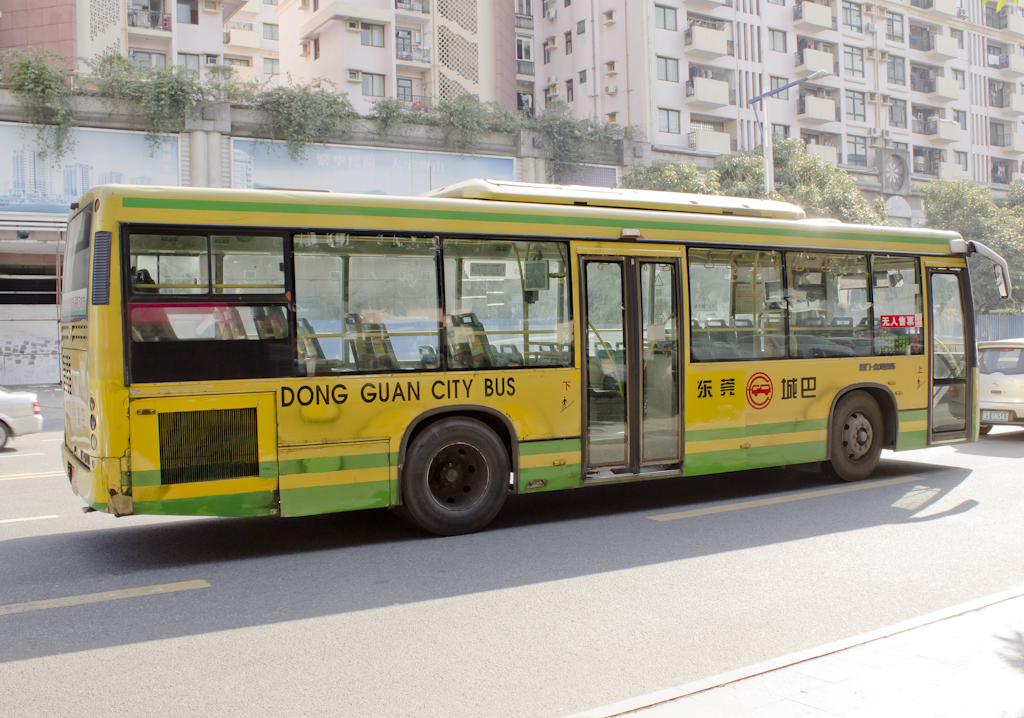 A yellow and green Dongguan city bus parked on a street with apartment buildings in the background.