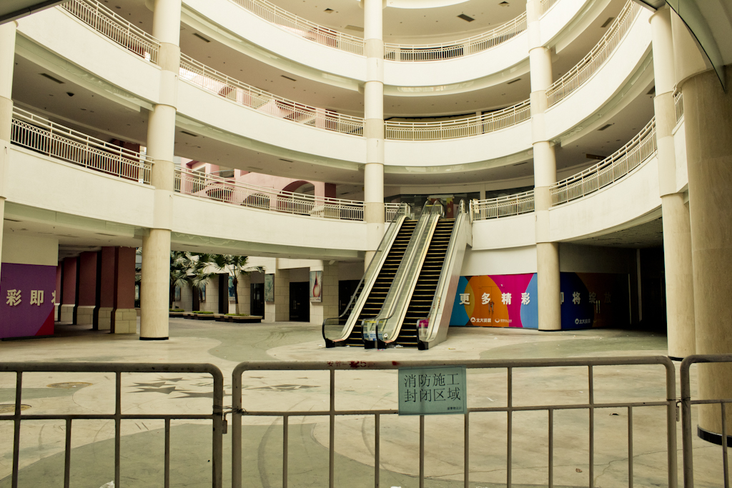 Empty shopping mall gallery with still escalators and closed storefronts in New South China Mall.