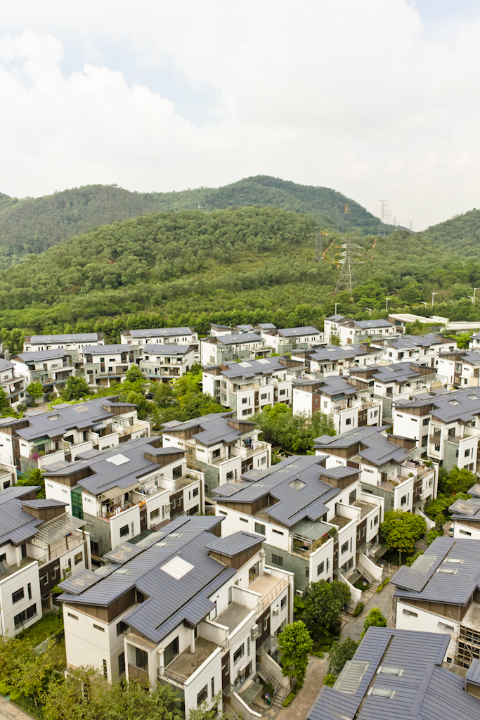 Aerial view of residential buildings with dark roofs in Dynatown, Dongguan, with forested hills in the background.
