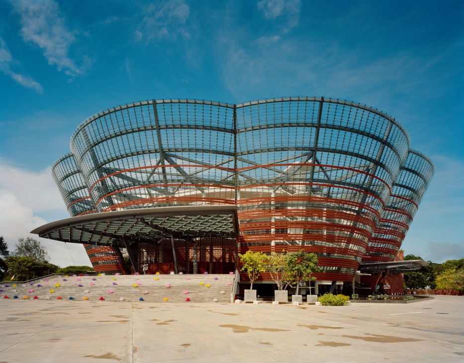 Modern circular building with glass and red steel framework under blue sky, Lotus Theatre in Colombo.