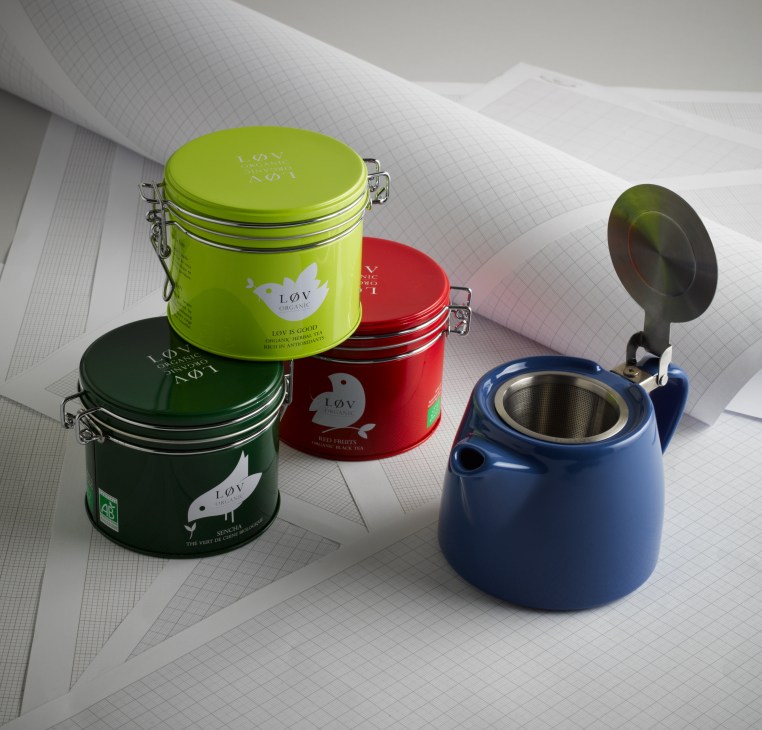 Løv Organic tea tins in green, red and black with metal clasps alongside a blue teapot with infuser.