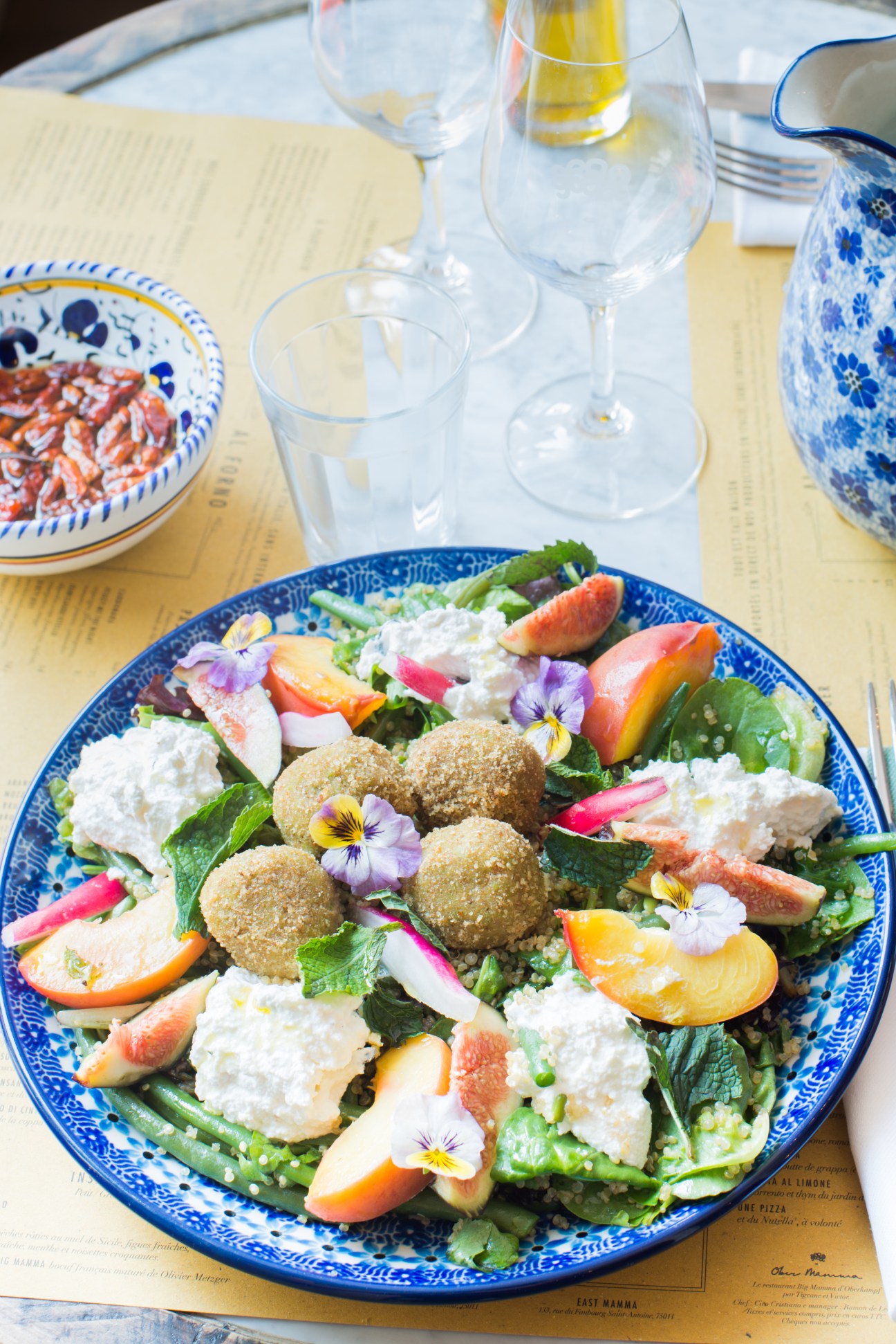 A colorful salad with falafel, greens, citrus slices, edible flowers and white cheese on a blue-patterned plate at Ober Mamma, Paris.