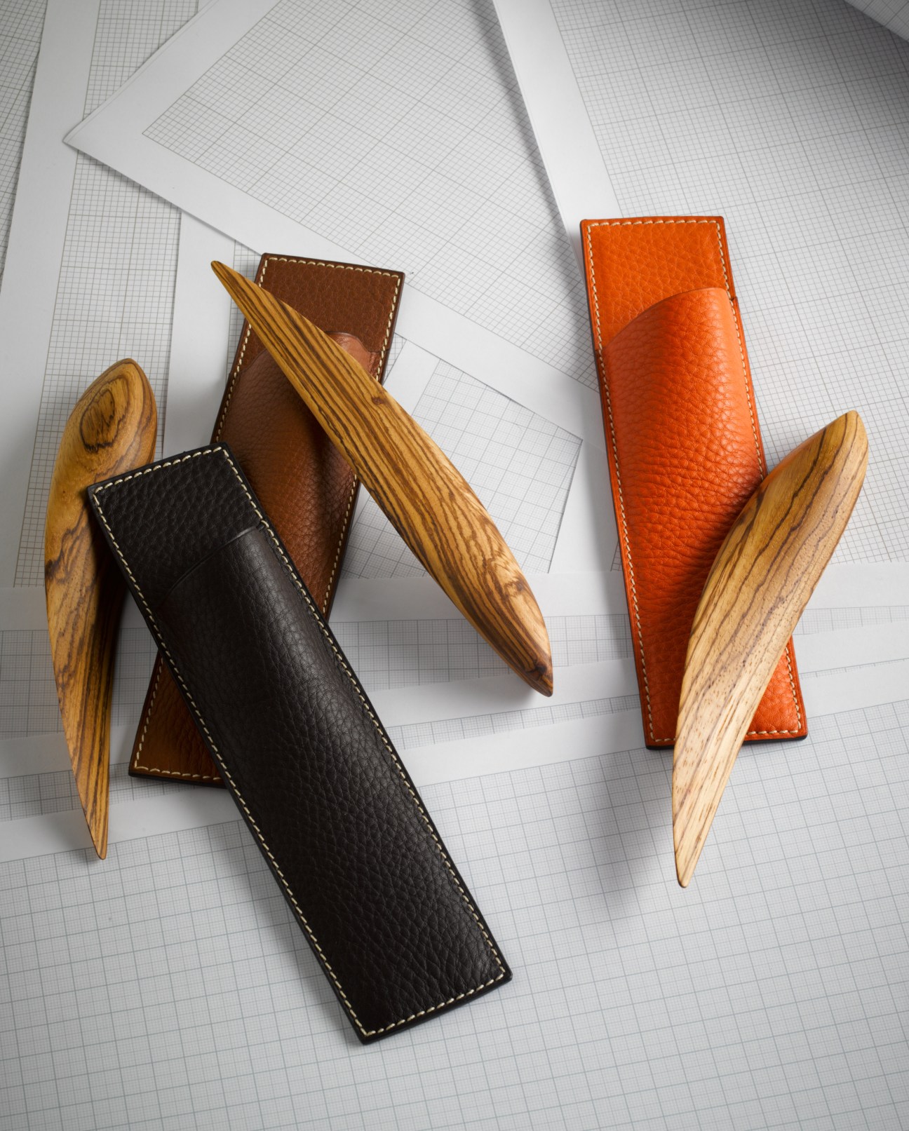 Lupa letter openers with wooden handles and leather holders in brown, black and orange on gridded paper.