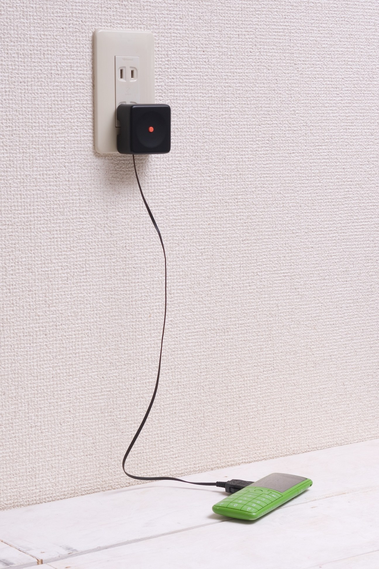 Yota Kakuda's tape measure-inspired phone charger plugged into wall outlet above green phone.