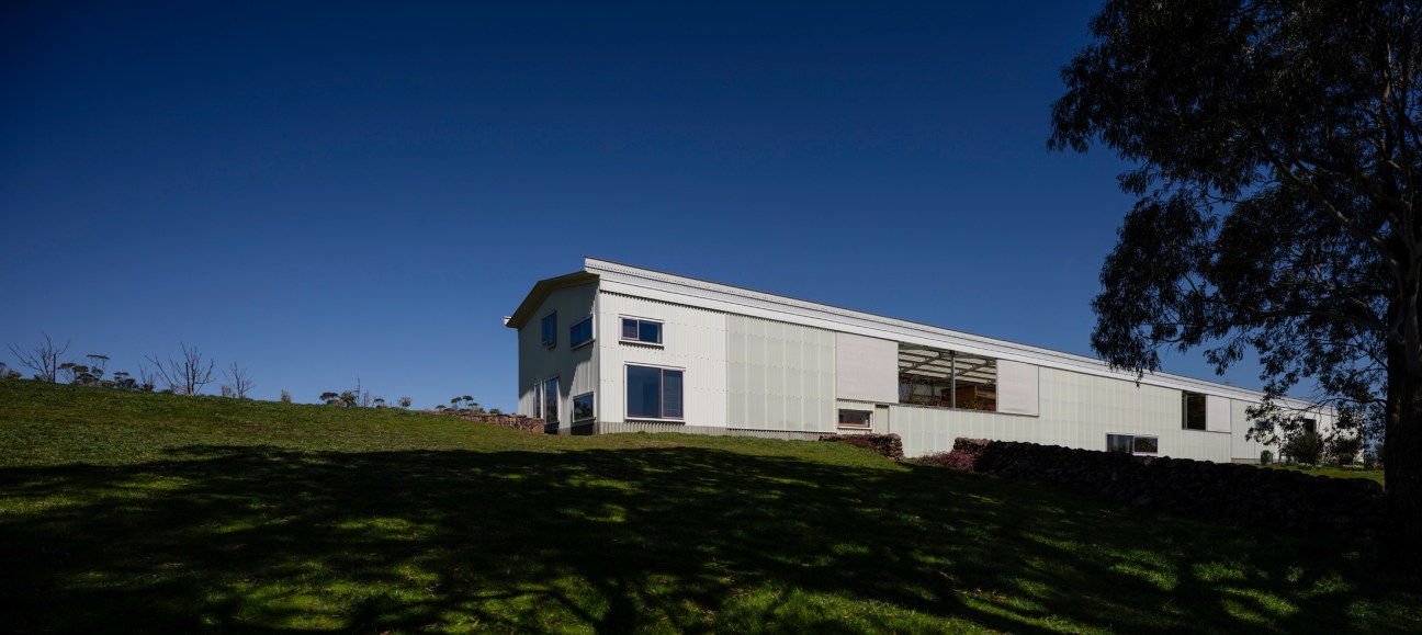 Modern white corrugated metal house sits on rolling green hillside against deep blue twilight sky