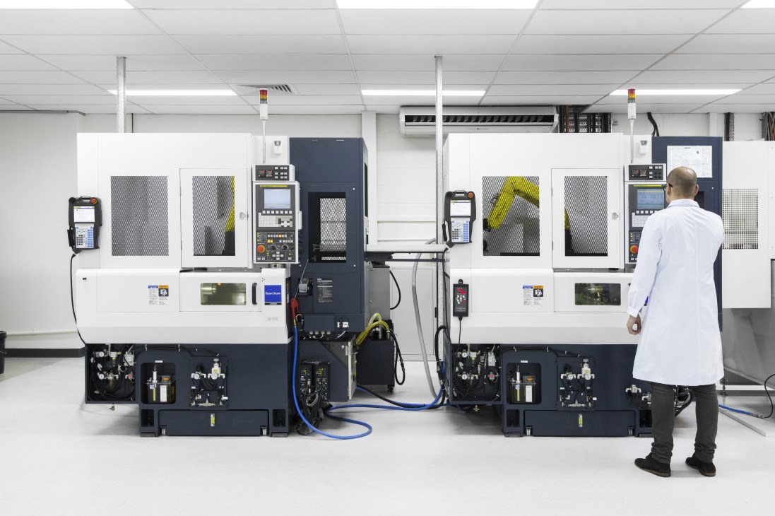 Worker in white coat monitoring advanced CNC machinery at Røde Microphones manufacturing facility